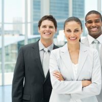 Beautiful young businesswoman and her two colleagues smile while posing for the camera in an office building. Horizontal shot.