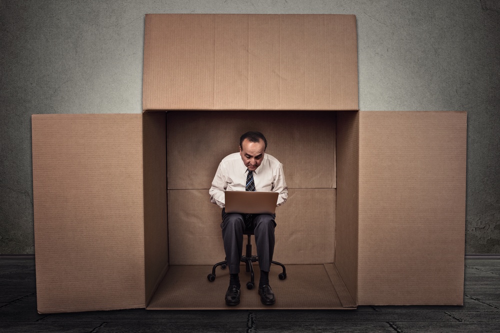 Limitations poor communication of corporate life. Portrait corporate middle aged man working on laptop sitting on chair inside carton box in empty office room.jpeg